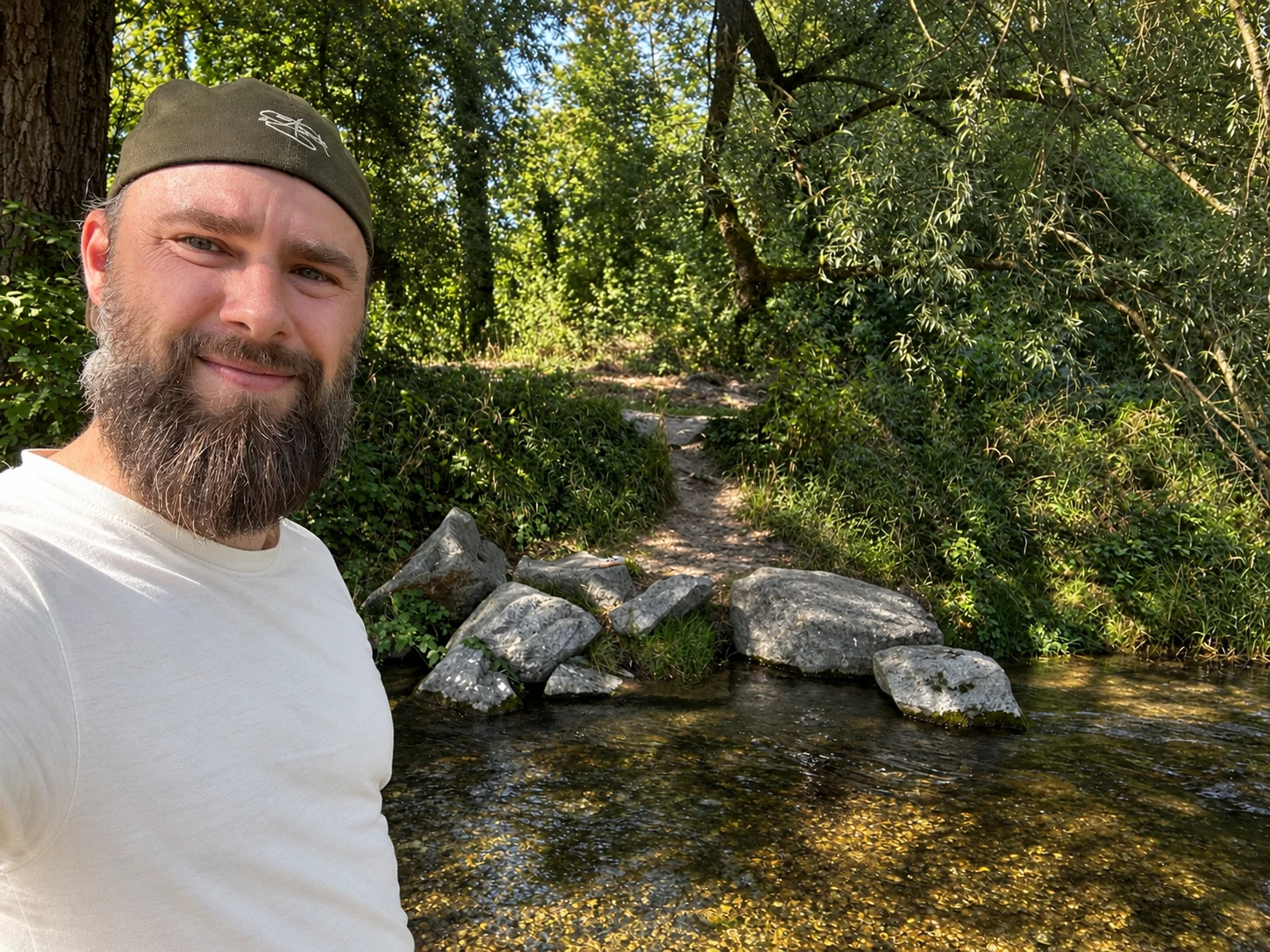 Lasse mit Mütze und Bart an einem Bach im Wald